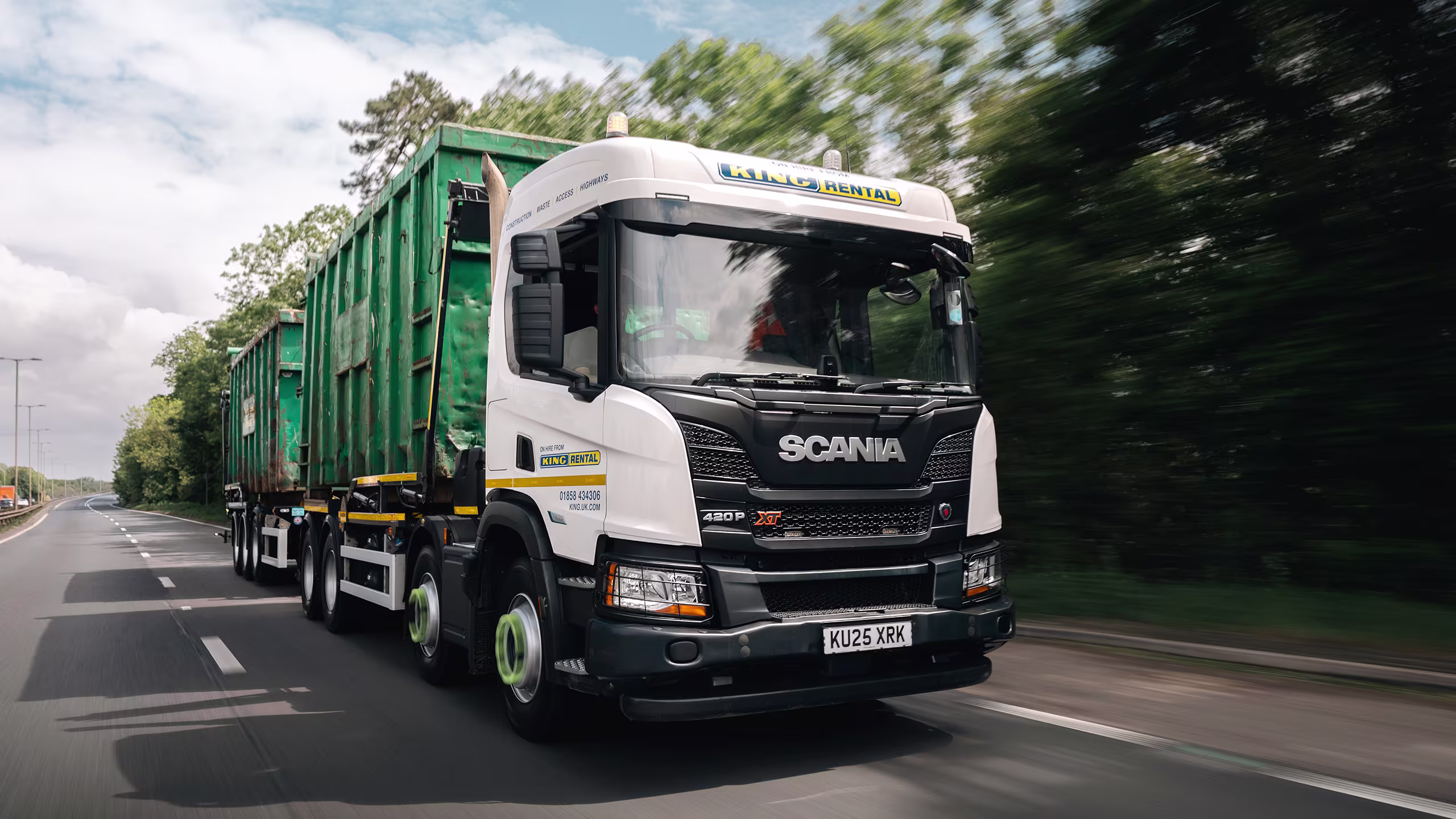 King Rental hook loader vehicle transporting bulk waste bins on a highway.