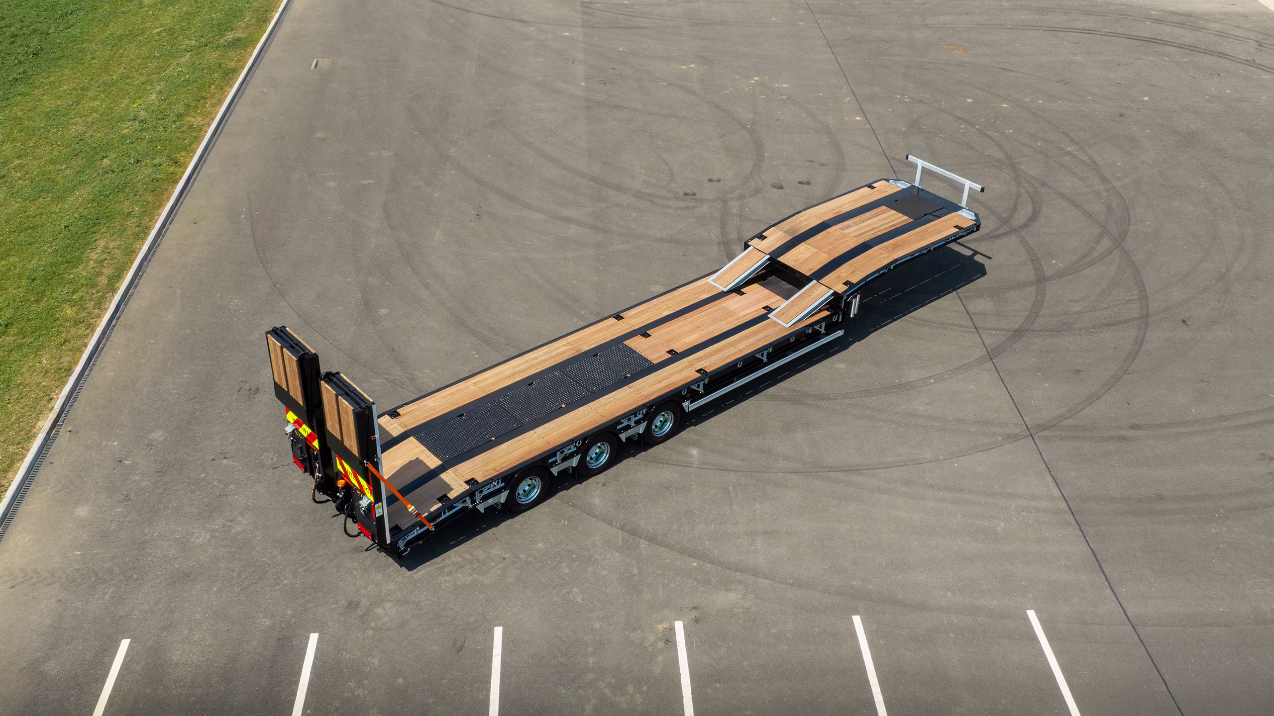 Aerial view of a long flatbed trailer with a wooden deck parked on an empty asphalt lot.